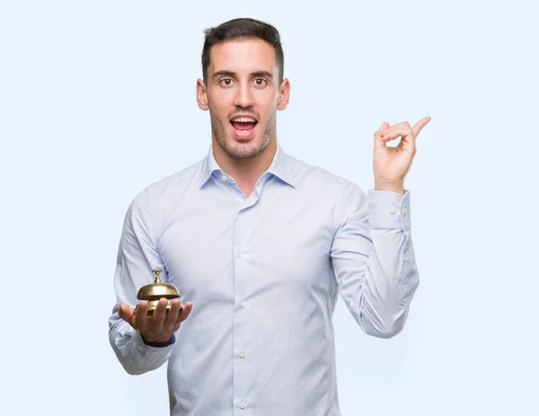 Handsome Young Man Holding Hotel Ring Bell Very Happy Pointing — Stock Photo, Image