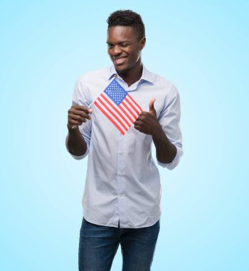 Ok işareti, başparmak ile parmak, mükemmel işareti yapıyor kocaman bir gülümseme ile ABD bayrağı mutlu tutan genç Afro-Amerikan adam