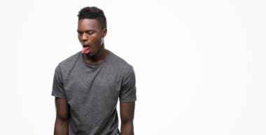 Gri t-shirt yapışma dil giyen genç Afro-Amerikan adam out komik ifade ile mutlu. Duygu kavramı.