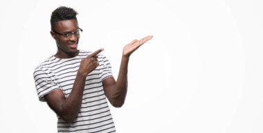 Gözlük ve hayrete ve el ile sunulması ve parmak ile işaret ederken kameraya gülümseyen lacivert t-shirt giyen genç Afro-Amerikan adam.