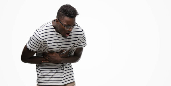 Young african american man wearing glasses and navy t-shirt with hand on stomach because nausea, painful disease feeling unwell. Ache concept.