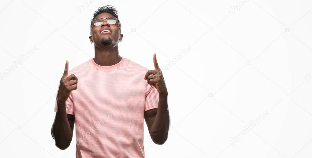 Young african american man wearing pink t-shirt amazed and surprised looking up and pointing with fingers and raised arms.