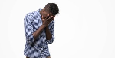 Genç Afro-Amerikan adam üzgün ifadeyle yüz eller ile ağlayarak süre kapsayan mavi tişört giyiyor. Depresyon kavramı.