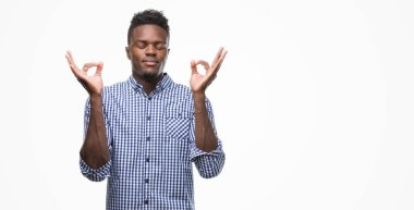 Mavi gömlek giymiş genç Afro-Amerikan adam rahatla ve gülümseyen gözlerle kapalı parmak jestle meditasyon yapıyor. Yoga kavramı.