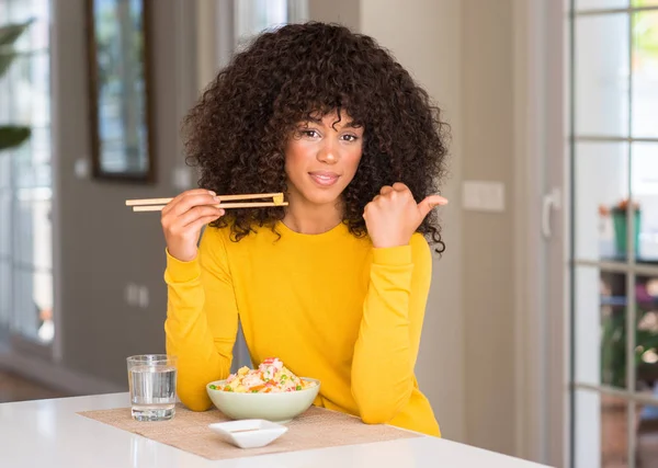 African american woman eating asian rice at home pointing with hand and finger up with happy face smiling