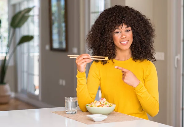 African american woman eating asian rice at home very happy pointing with hand and finger