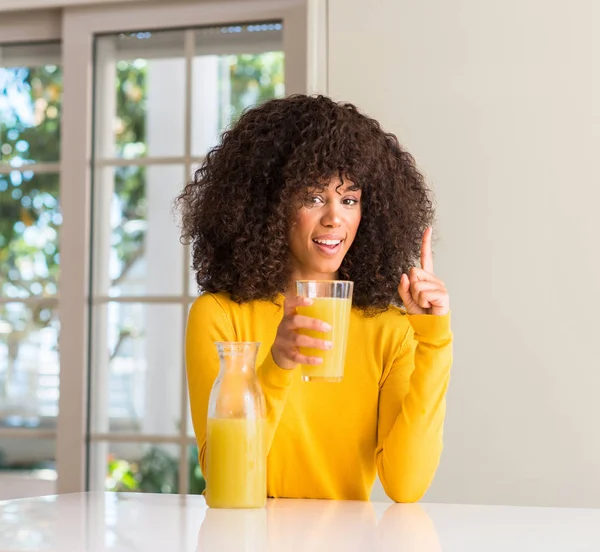 在家里喝健康果汁的非洲裔美国妇女惊讶于一个想法或问题指着一个快乐的脸 — 图库照片