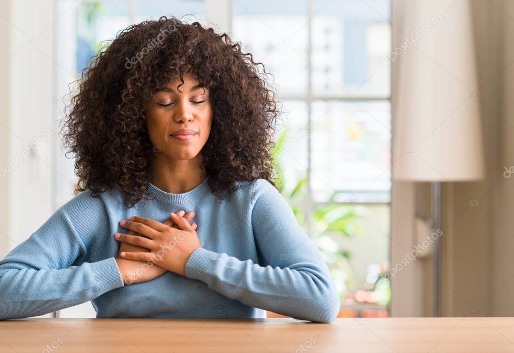 African american woman at home smiling with hands on chest with closed eyes and grateful gesture on face. Health concept.