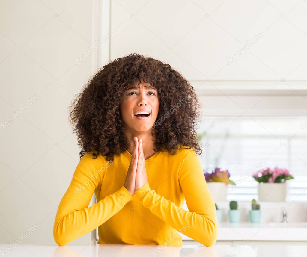 African american woman wearing yellow sweater at kitchen begging and praying with hands together with hope expression on face very emotional and worried. Asking for forgiveness. Religion concept.