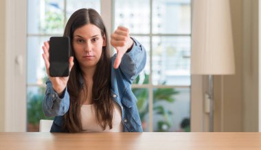 Akıllı telefon kullanan kızgın yüzü, eksi işareti aşağı antipati başparmak ile gösterilen, ret kavramı ile genç kadın