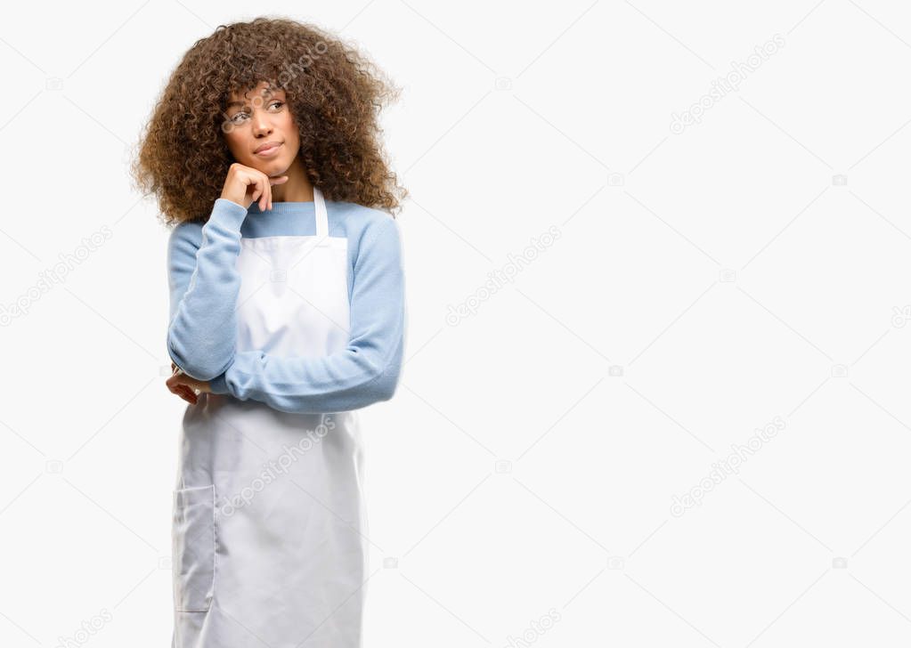 African american shop owner woman wearing an apron thinking and looking up expressing doubt and wonder