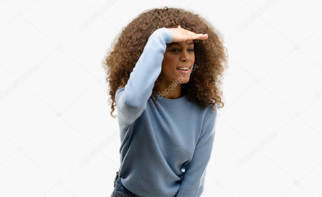 African american woman wearing a sweater very happy and smiling looking far away with hand over head. Searching concept.