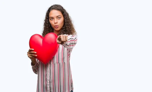 Młody Hiszpanin Kobieta Zakochana Trzymając Czerwone Serce Wskazując Palcem Aparatu — Zdjęcie stockowe
