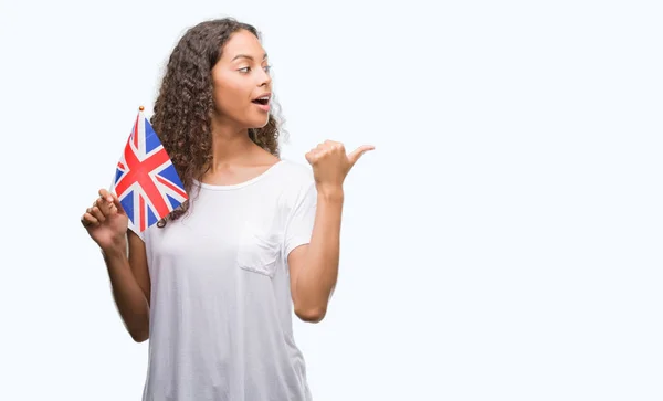 若いヒスパニックの女性をイギリスの旗を保持して指していると幸せそうな顔を笑顔で側まで親指で示す — ストック写真