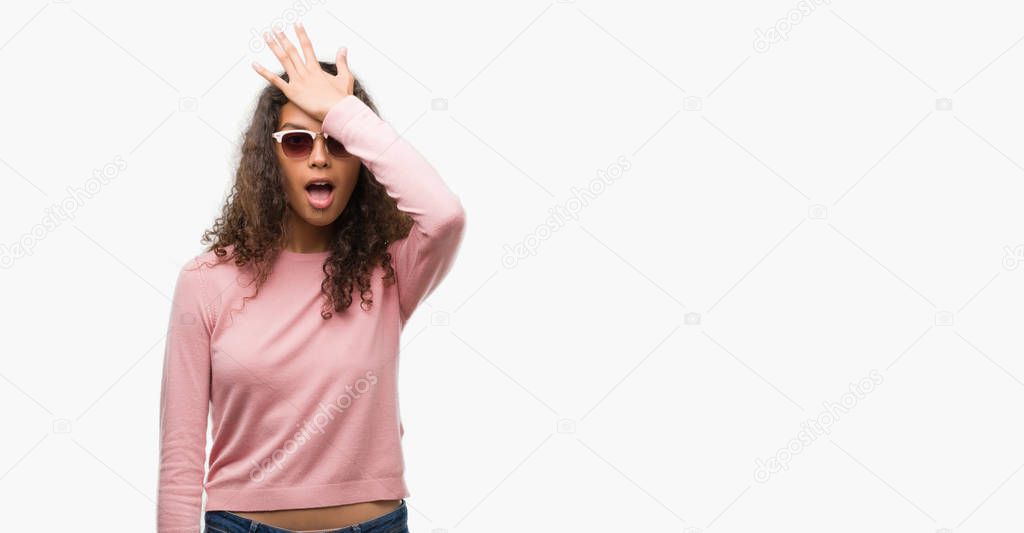Beautiful young hispanic woman wearing sunglasses surprised with hand on head for mistake, remember error. Forgot, bad memory concept.