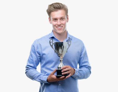 Genç yakışıklı sarışın adam ayakta ve diş gösterilen kendine güvenen bir gülümsemeyle gülümseyerek mutlu bir yüz ile bir kupa holding