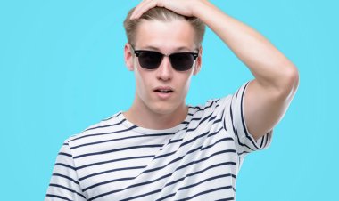 Genç yakışıklı sarışın adam giyen sunglasess kafasına, utanç ve sürpriz ile şok el ile vurguladı yüz, öfkeli ve sinirli. Korku ve hata için üzgün.