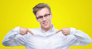 Yüzünde gülümseme ile kendinden emin görünüyorsun, kendini gururlu ve mutlu parmakları ile işaret genç yakışıklı sarışın adam.