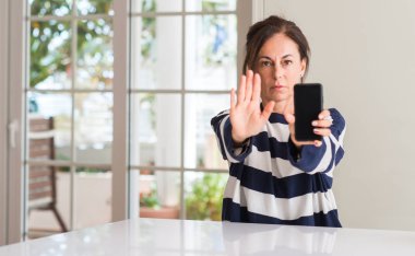 Açık eliyle dur işareti ile ciddi ve kendine güvenen ifade, savunma jest yapıyor akıllı telefon kullanan orta yaşlı kadın