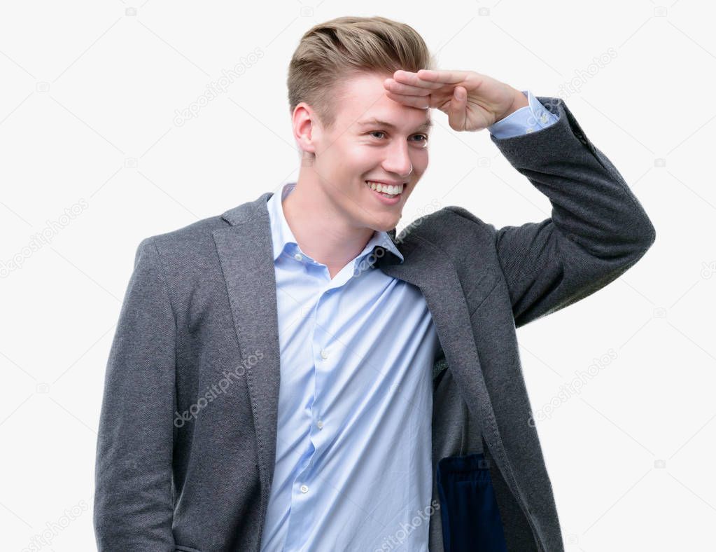 Young handsome blond business man very happy and smiling looking far away with hand over head. Searching concept.