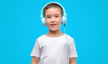 Koyu saçlı küçük çocuk müzik dinleme kulaklık daimi ve diş gösterilen kendine güvenen bir gülümsemeyle gülümseyerek mutlu bir yüz ile