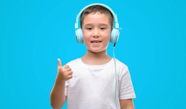 Koyu saçlı küçük çocuk müzik dinleme kulaklıklarla ok işareti, başparmak ile parmak, mükemmel işareti yapıyor kocaman bir gülümseme ile mutlu