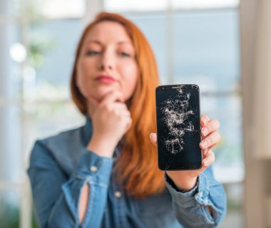 Kırık smartphone ciddi bir yüz düşünme hakkında soru, çok karışık fikir tutan Kızıl saçlı kadın