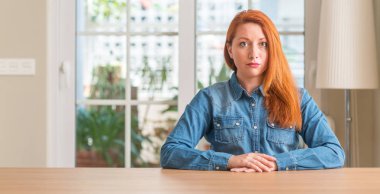 Yüzünde ciddi bir ifade ile Kızıl saçlı kadın evde. Basit ve doğal kameraya bakıyor.