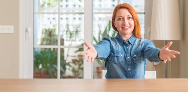 Kızıl saçlı kadın evde sarılmak için kollarını açarak gülümseyen kamera bakıyor. Neşeli ifade kucaklayan mutluluk.