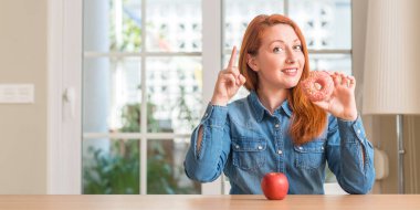 Kızıl saçlı kadın elma ve bir fikir ya da soru işaret parmağı gülen yüz, bir numara ile sürpriz çörek arasında seçer