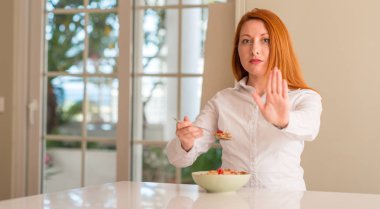 Kızıl saçlı kadın yeme tahıllar ile ahududu evde dur işareti ciddi ve kendine güvenen ifade ile yapıyor açık el ile jest savunma.