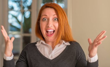 Kızıl saçlı kadın evde çok mutlu ve heyecanlı, kocaman bir gülümseme ile çığlık ve ellerini kaldırdı zaferini kutluyor kazanan ifade