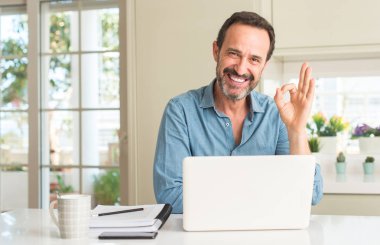 Dizüstü evde kullanan orta yaş adam parmak, mükemmel sembolü ile ok işareti yapıyor