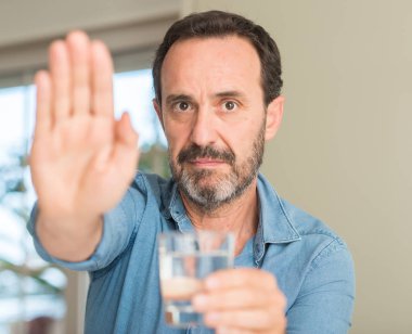 Bir bardak su ile içme orta yaş erkek açık el dur işareti ile ciddi ve kendine güvenen ifade, savunma hareketi yapıyor