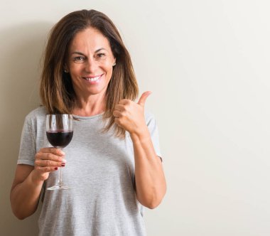 Ok işareti, başparmak ile parmak, mükemmel işareti yapıyor kocaman bir gülümseme ile mutlu bir bardak kırmızı şarap içme orta yaş kadın