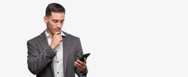 Yakışıklı genç adam akıllı telefon ciddi bir yüz düşünme soru hakkında çok kullanarak fikir karışık