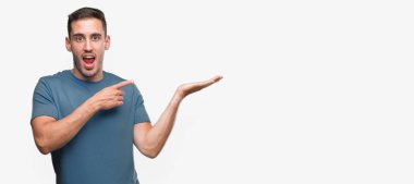 Hayret ve el ile sunulması ve parmak ile işaret ederken kameraya gülümseyen yakışıklı genç casual adam.