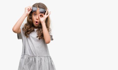 Esmer Latin kız ok jest sürpriz yüz, göz parmaklarının arasından seyir şok yapıyor güneş gözlüğü takıyor. İmansız ifade.