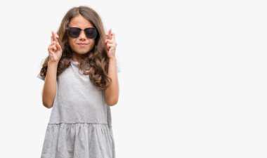 Esmer Latin kız umut ve gözleri kapalı geçiş parmaklarıyla gülümseyen güneş gözlüğü takıyor. Şans ve batıl kavramı.