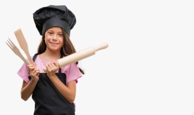 Esmer Latin kız ayakta ve diş gösterilen kendine güvenen bir gülümsemeyle gülümseyerek mutlu bir yüz ile aşçı üniforması