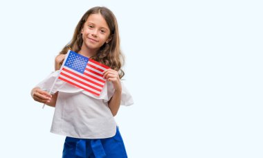 Esmer Latin kız ayakta ve diş gösterilen kendine güvenen bir gülümsemeyle gülümseyerek mutlu bir yüz ile Amerika Birleşik Devletleri bayrağı tutarak