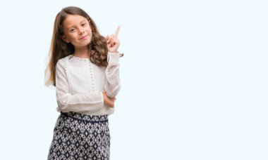 Esmer Latin kız kameraya bakarak yan el ve parmak ile işaret yüzünde kocaman bir gülümseme ile.