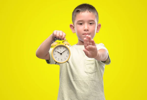 小孩子手持闹钟用张开的手做停止标志以严肃和自信的表达 防御手势 — 图库照片