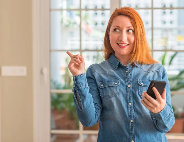Κοκκινομάλλης Γυναίκα Χρησιμοποιώντας Smartphone Στο Σπίτι Πολύ Χαρούμενος Δείχνοντας Χέρι — Φωτογραφία Αρχείου