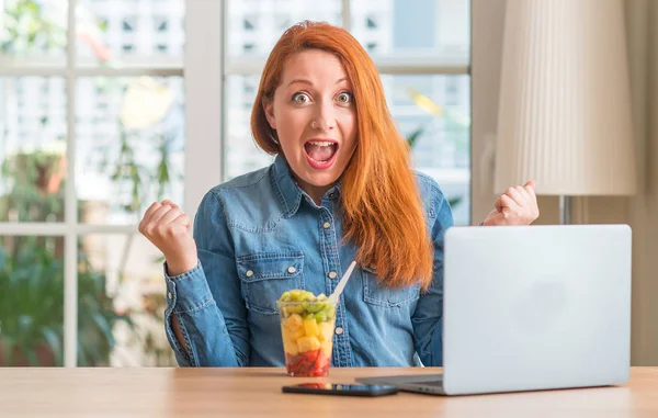 Donna Rossa Utilizzando Computer Portatile Mangiare Frutta Casa Urlando Orgoglioso — Foto Stock