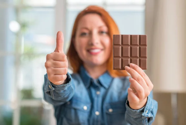 赤毛を持つ女性チョコレートバー自宅幸せ笑顔の サイン 優秀な兆候を親指をやって — ストック写真