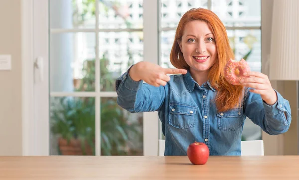 红发女人在苹果和甜甜圈之间选择非常愉快指向用手和手指 — 图库照片