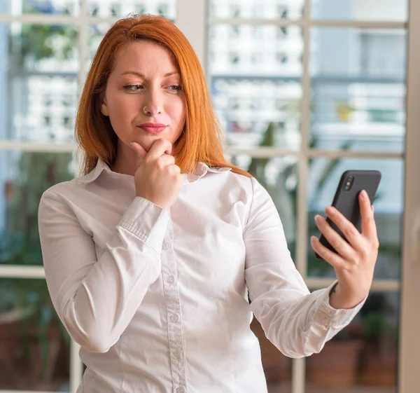 红发女人用智能手机在家认真面对问题 非常困惑的想法 — 图库照片