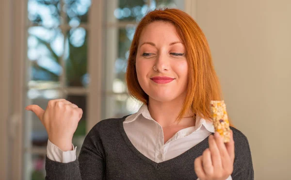 Rothaarige Frau Isst Müsliriegel Hause Und Zeigt Mit Der Hand — Stockfoto