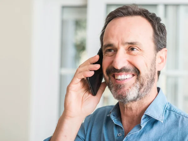 Ayakta ve diş gösterilen kendine güvenen bir gülümsemeyle gülümseyerek mutlu bir yüz ile akıllı telefon kullanan orta yaş adam